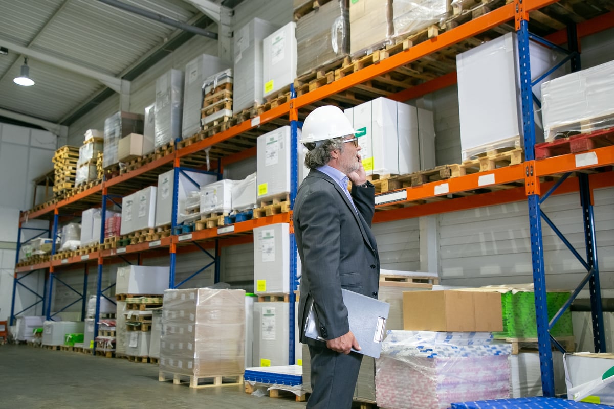 focused-ceo-formal-suit-hardhat-standing-warehouse-talking-mobile-phone